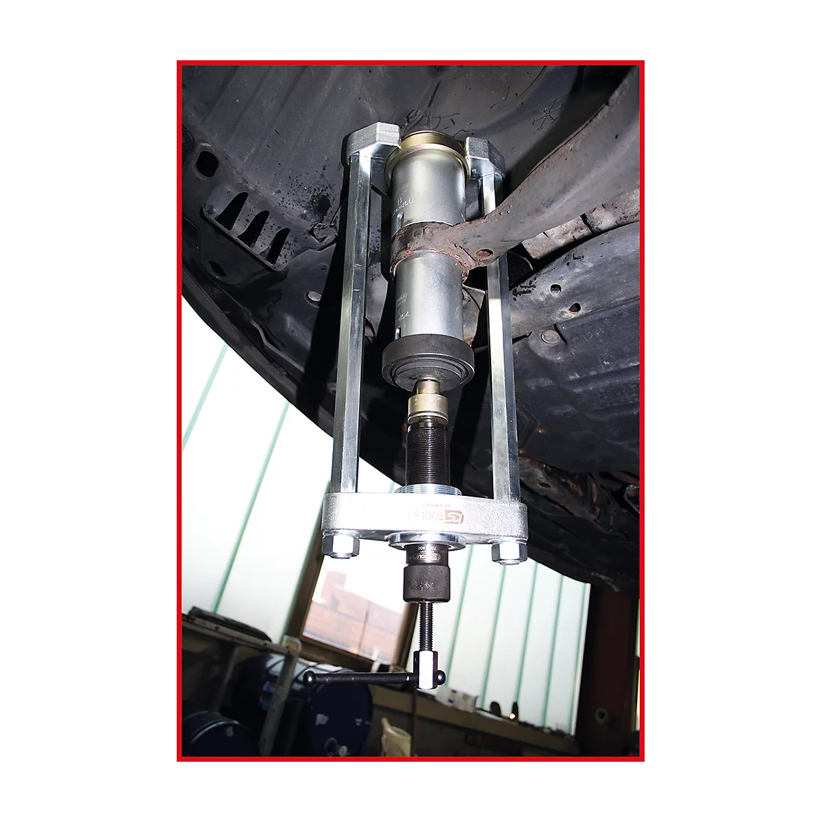 Werkzeug zur Demontage eines Stoßdämpfers. Ein silbernes Werkzeug ist am Fahrwerk eines Autos befestigt.